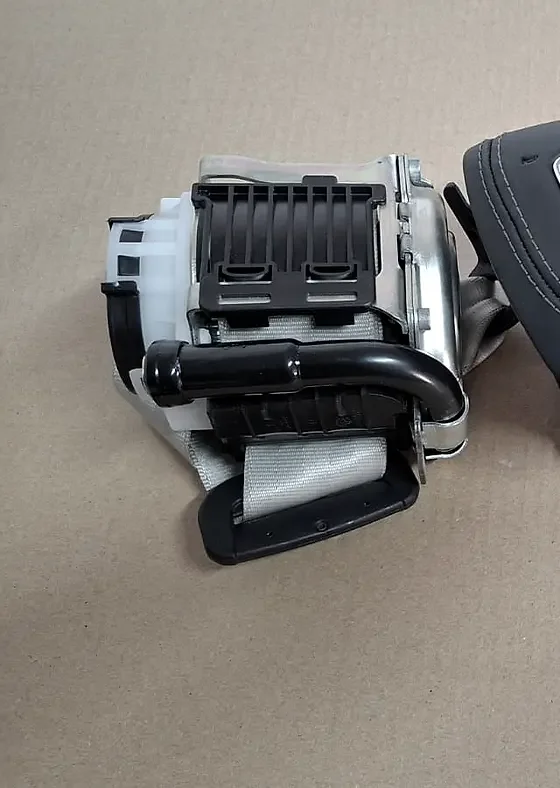 A seat belt retractor with its black belt on a cardboard sheet