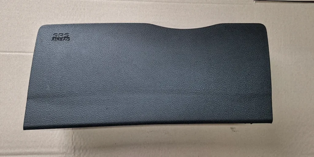 Black passenger airbag cover with SRS airbag lettering lying on cardboard